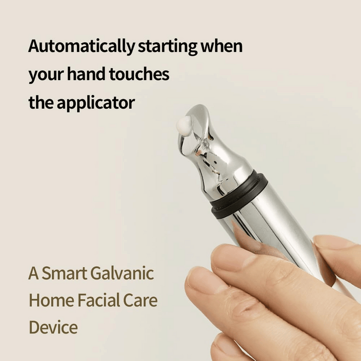 Närbild på en hand som håller i en galvanisk applikator för ögonkräm med automatisk startfunktion vid beröring. Text på bilden beskriver funktionen och enheten som ett smart hemverktyg för ansiktsvård.