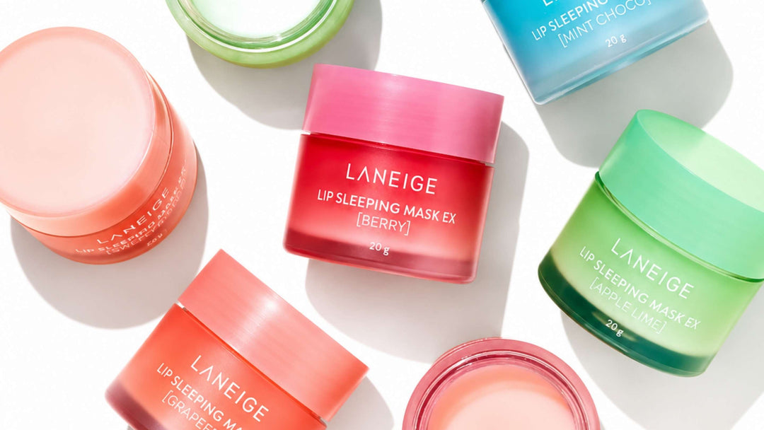 Bilden visar två burkar av LANEIGE Lip Sleeping Mask, en med smak av pepparmint och en annan med smak av karamelliserat äpple. Produkterna är snyggt placerade mot en kontrasterande bakgrund som framhäver deras färger och texturer.