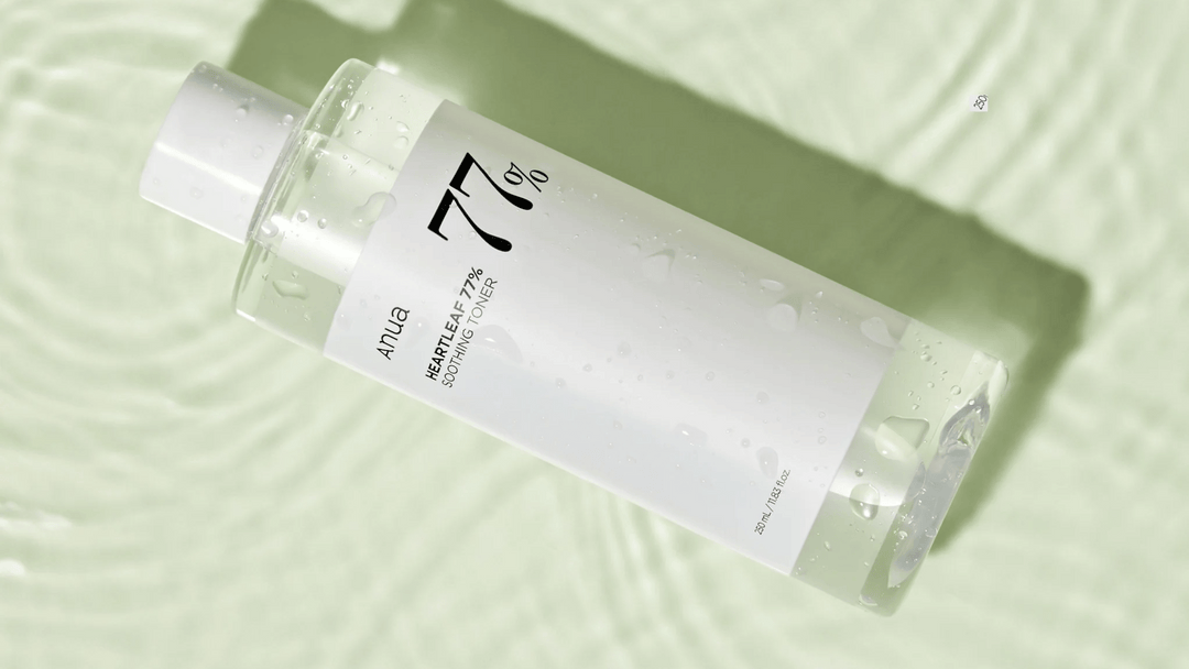 En vit flaska Anua Heartleaf 77% Soothing Toner ligger på en vågig grön yta, täckt av vattendroppar.