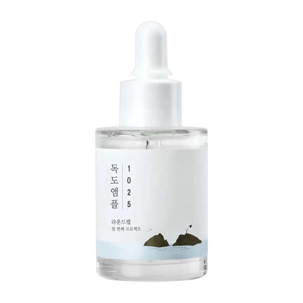 En gjennomsiktig flaske med 1025 Dokdo Ampoule ansiktsserum, dekorert med minimalistisk havstema, på hvit bakgrunn.
