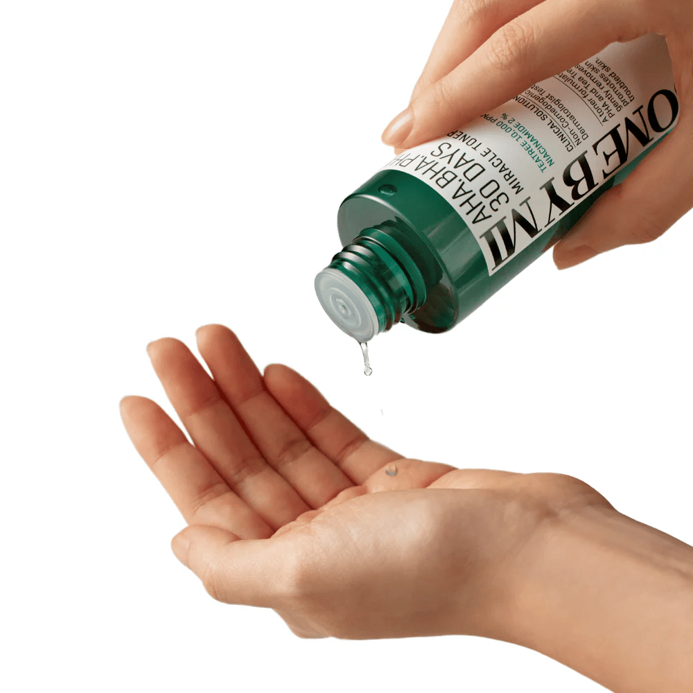 En hånd holder en grønn flaske med teksten "AHA, BHA, PHA 30 Days Miracle Toner" og presser ut en klar væske i den andre håndens håndflate, klar til bruk.