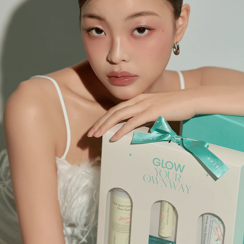 Modell med elegant sminke holder i AXIS-Y:s “Glow Your Own Way”-gaveboks – en stilren Hudpleiesett perfekt som gave til deg selv eller noen du er glad i.