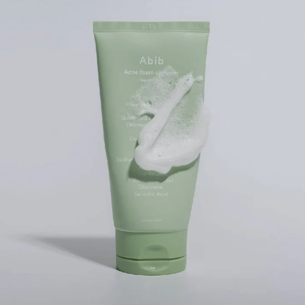 Grønn tube med Abib Acne Foam Cleanser Heartleaf, dekket av et hvitt skum som illustrerer den skummende rensende effekten. Produktet inneholder hjertebladekstrakt og salisylsyre for akneutsatt hud.