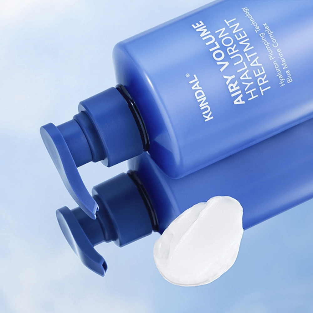 KUNDAL Airy Volume Hyaluron Treatment i blå pumpeflaske liggende, med hvit kremprodukt synlig ved siden av.