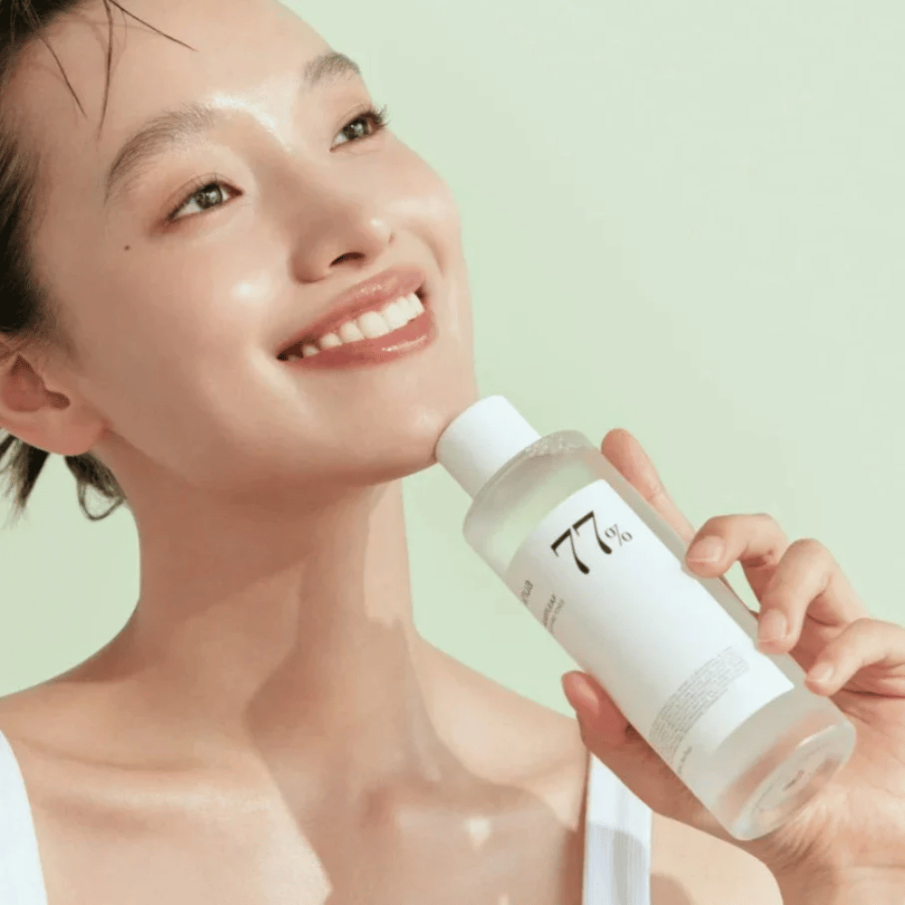 En kvinne beroliger sin sensitive hud med en flaske Heartleaf 77% Soothing Toner fra Anua, som inneholder kameleonblad-ekstrakt.