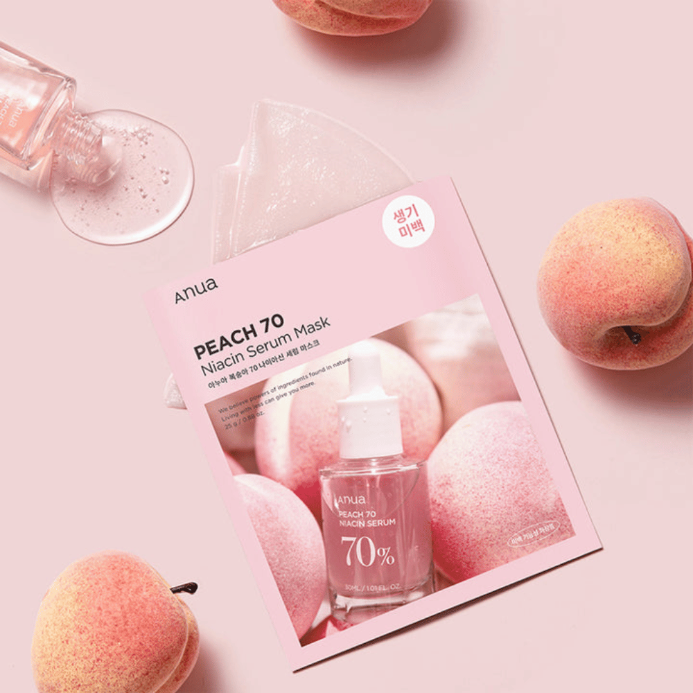 Et bilde av Anua PEACH 70 Niacin Serum Mask, omgitt av ferskener og en flaske serum. Bildet har en myk rosa bakgrunn, som kompletterer den rosa emballasjen og fremhever produktet og ingrediensene.