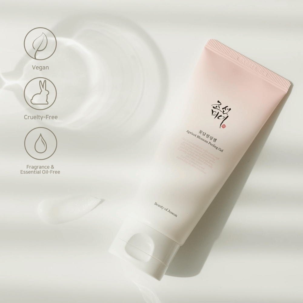 En tube med Apricot Blossom Peeling Gel ligger på en reflekterende overflate med ikoner som indikerer at produktet er vegansk, dyrevennlig og fri for duft og eteriske oljer.