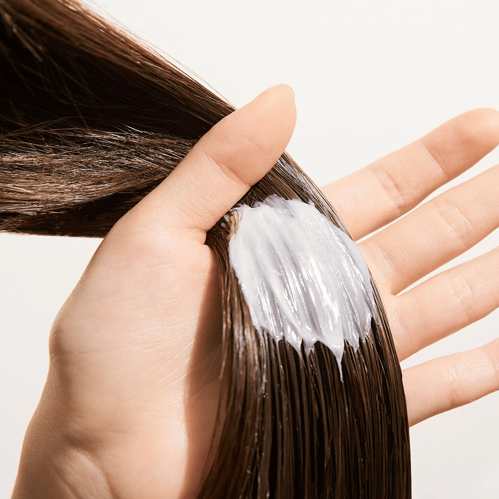Hånd påfører Nature Republic Argan Essential Moisture Repairing Hair Mask i vått hår – fuktighetsgivende maske som styrker og mykgjør håret.