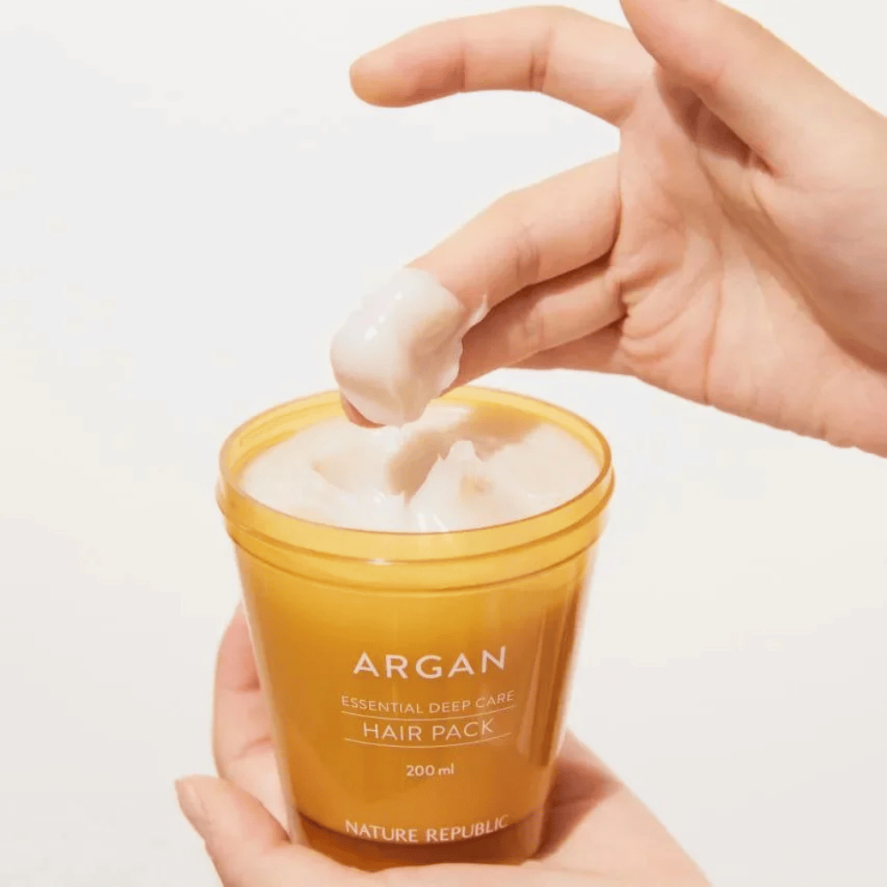 Hånd tar opp den kremete formelen fra Nature Republic Argan Essential Moisture Repairing Hair Mask – intensiv næring for tørt hår.