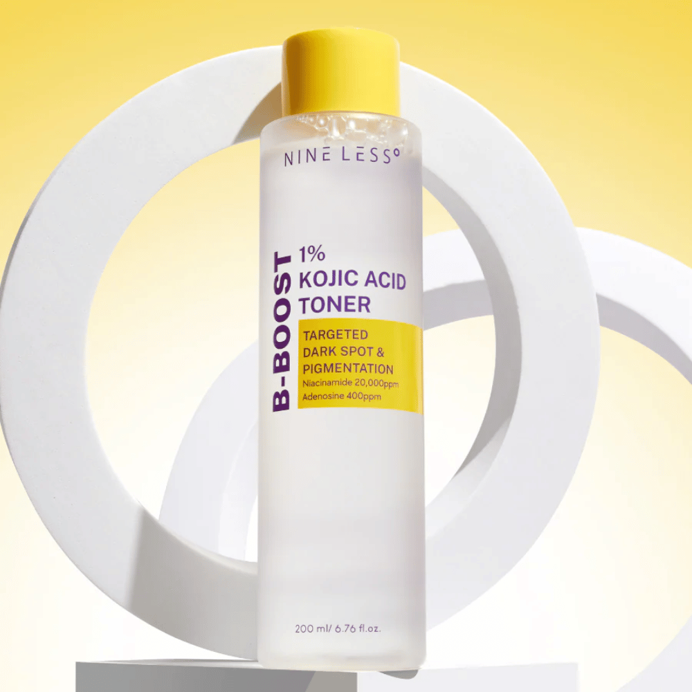NINE LESS B-Boost 1% Kojic Acid Toner stående mot gul bakgrunn med teksten "Targeted Dark Spot & Pigmentation". Hudtone-utjevnende toner med niacinamid og adenosin.