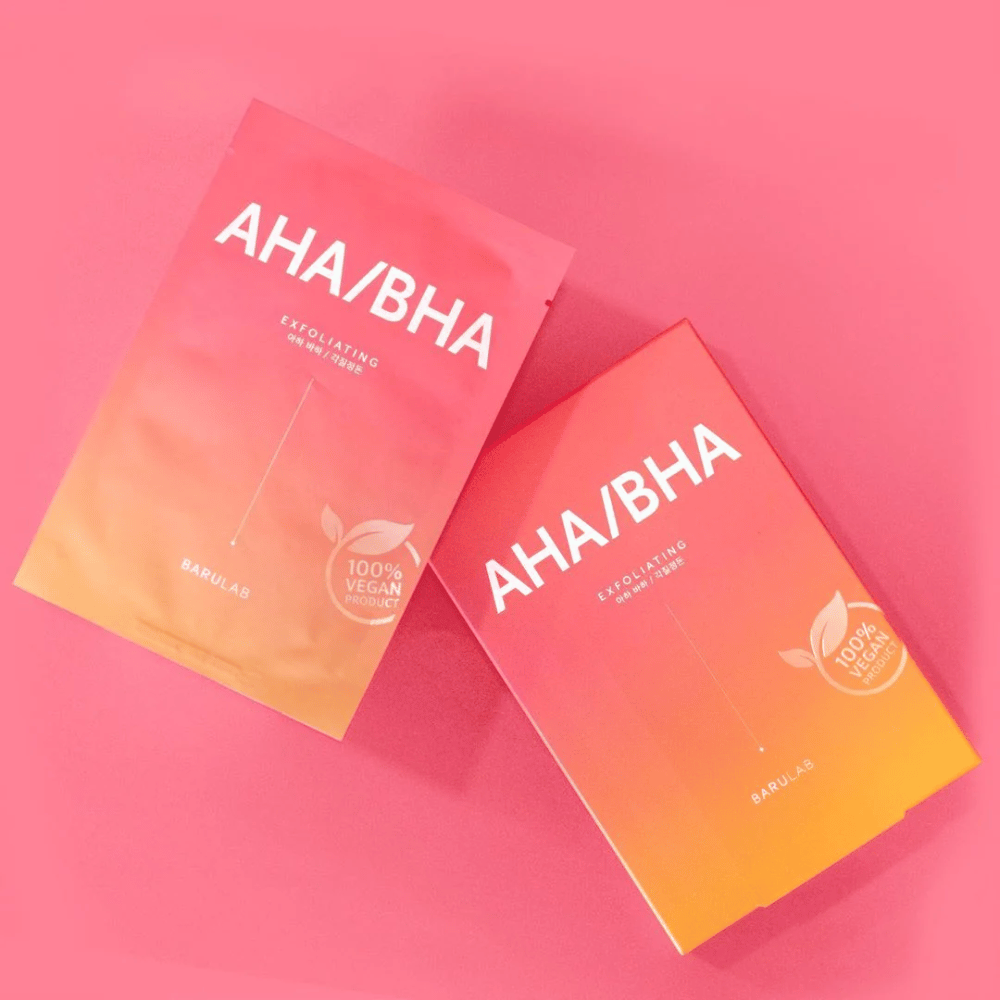To produkter fra BARULAB, en i en pose og en i en eske, begge merket med "AHA/BHA" og "Exfoliating" mot en rosa bakgrunn. Produktene er merket som "100% Vegan Product".