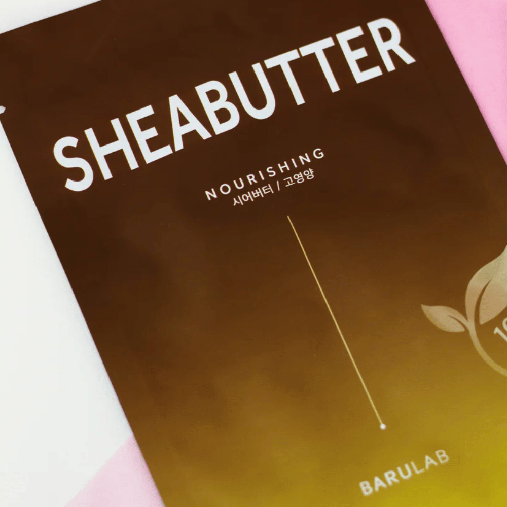 Et nærbilde av en pakke med BARULAB "SHEABUTTER Nourishing" maske. Produktet er merket som "100% Vegan Product" og har en fargegradient fra mørkebrun til lys brun.