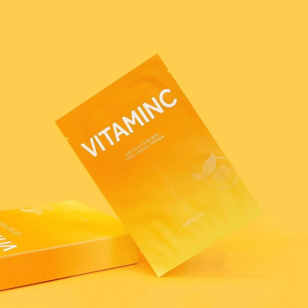 En haug av pakker med BARULAB "VITAMINC Brightening" masker, alle merket som "100% Vegan Product". Pakningene har en fargetone i ulike nyanser av oransje og gult, plassert mot en ensartet gul bakgrunn.