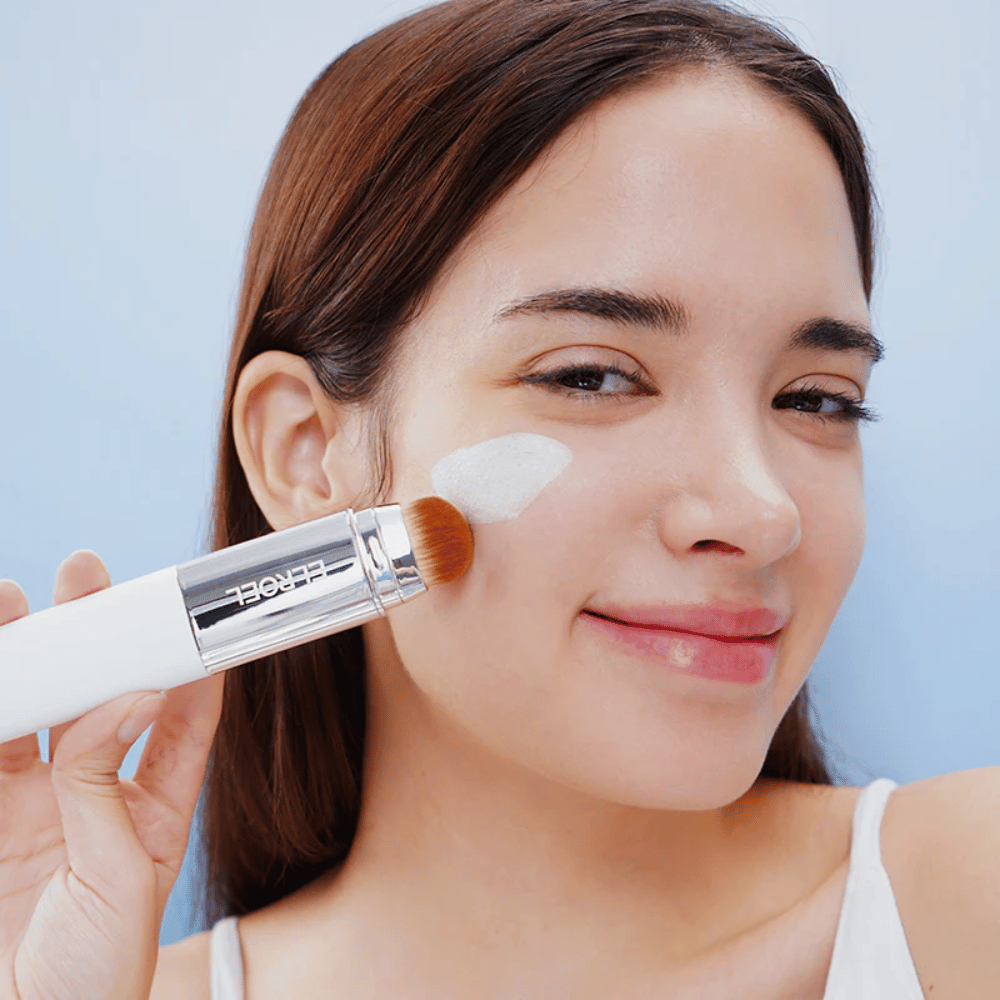 Modell påfører ELROEL Blanc Cover Cream Stick concealer på kinnet med innebygd børste for naturlig og jevn dekning.