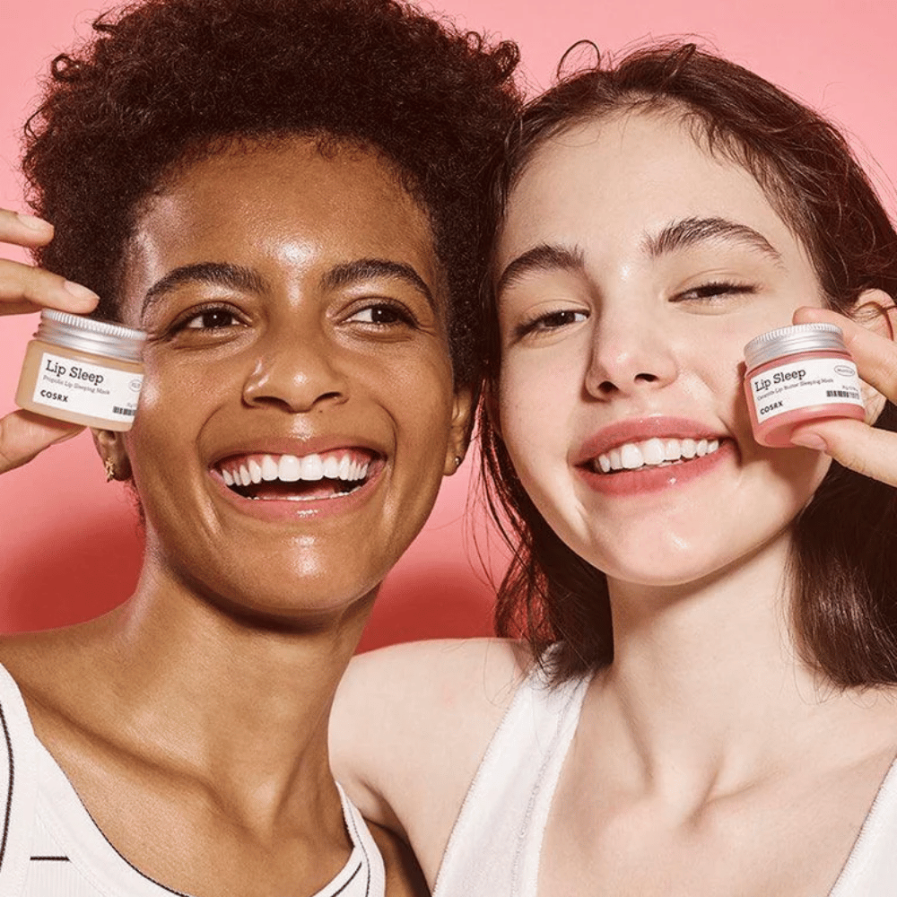 To personer smiler og holder opp COSRX Lip Sleep-krukker. Bildet formidler myke, fuktede lepper og produktets naturlige glødgivende effekt.