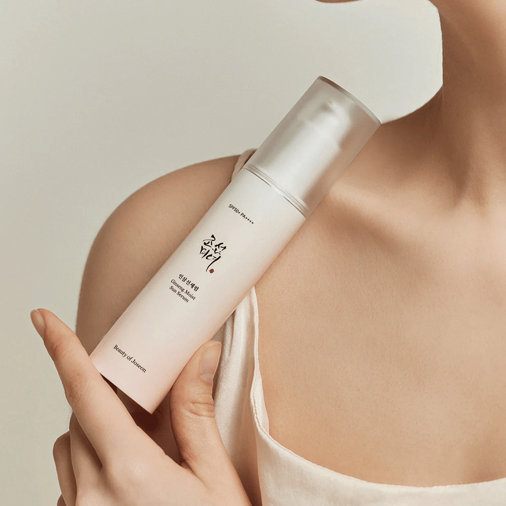 En kvinne som holder en flaske Beauty of Joseon's Ginseng Moist Sun Serum SPF 50+ PA++++, som gir SPF 50+ PA++++ beskyttelse og hudpleiefordeler.