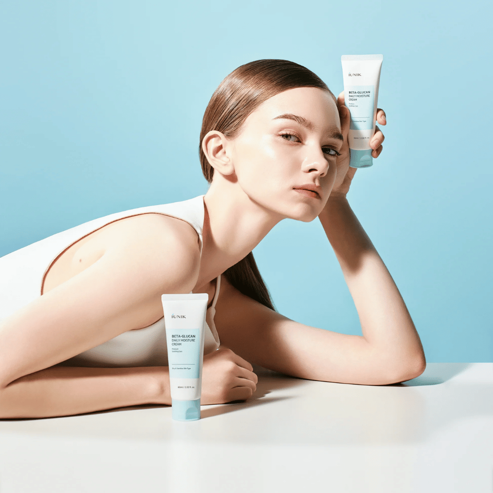 Livsstilsbilde der en modell poserer med iUNIK Beta-Glucan Daily Moisture Cream mot en lyseblå bakgrunn. Bildet formidler en ren, frisk og fuktighetsgivende følelse samtidig som produktet eksponeres tydelig.