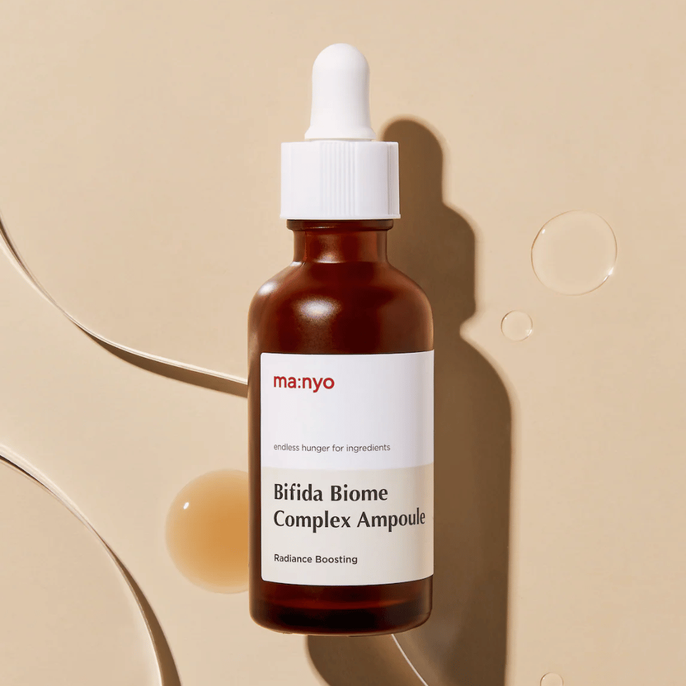 Stilrent produktbilde av ma:nyo Bifida Biome Complex Ampoule med fokus på flaskedesign og serumdråper i bakgrunnen.
