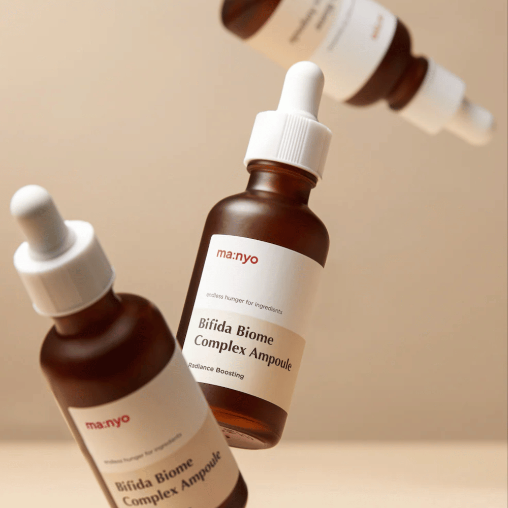 Produktbilde med flere svevende flasker av ma:nyo Bifida Biome Complex Ampoule mot beige bakgrunn som gir en moderne og minimalistisk følelse.