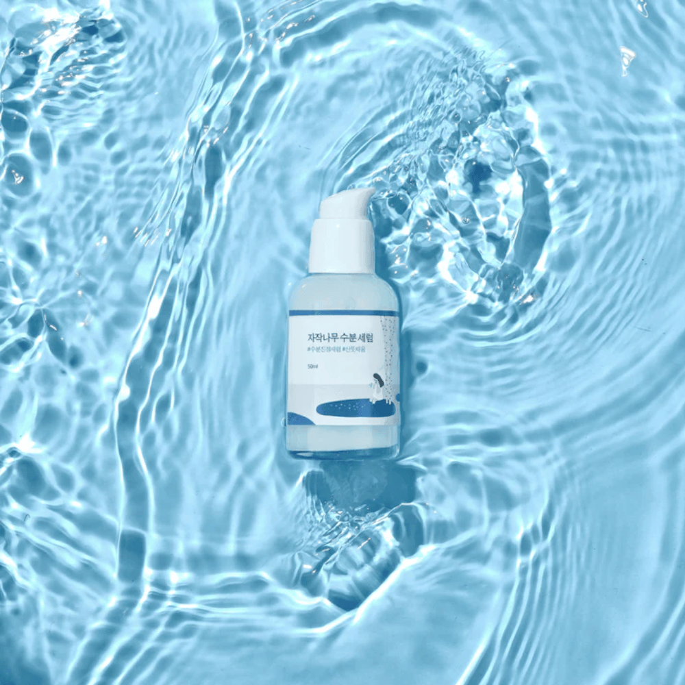 Round Lab Birch Juice Moisturizing Serum i pumpeflaske flytende på blått vann med sollysrefleksjoner.