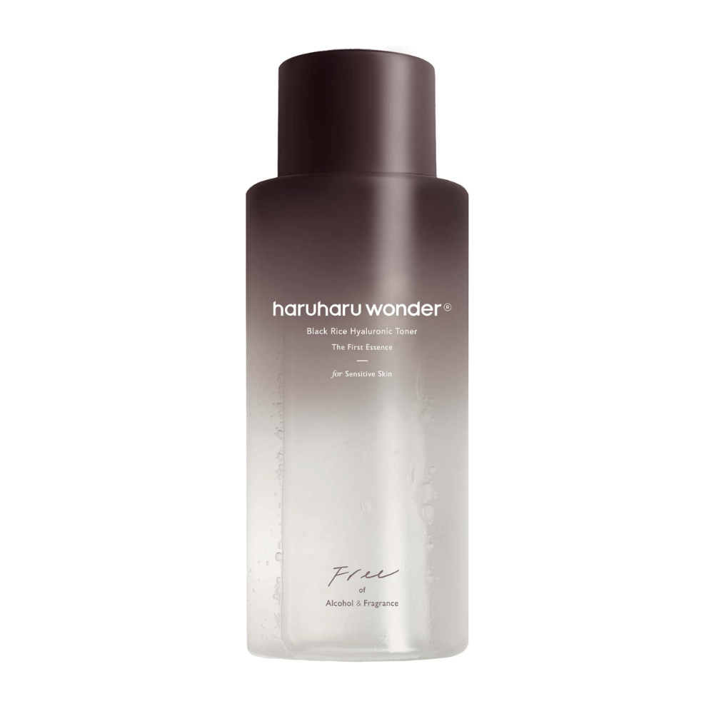 En flaske av haruharu wonder Black Rice Hyaluronic Toner The First Essence, med mørkebrun til gjennomsiktig gradient og teksten "Free of Alcohol & Fragrance", på hvit bakgrunn.