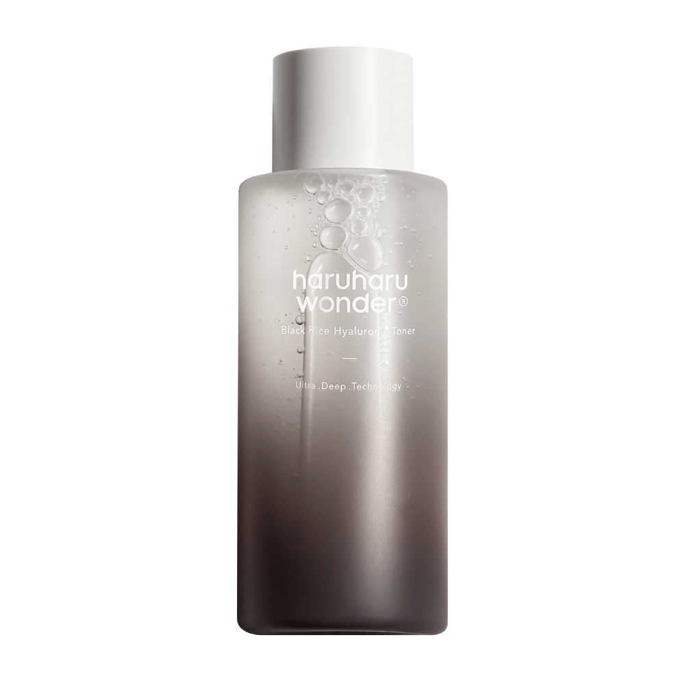 En flaske av haruharu wonder Black Rice Hyaluronic Toner med en grå til hvit fargegradient og vanndråper på overflaten, mot en hvit bakgrunn.