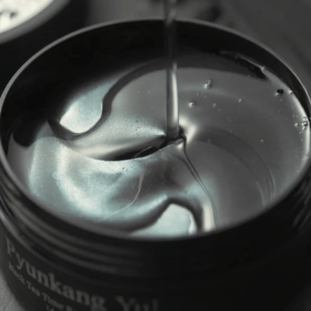 Nærbilde av svarte hydrogel eye patches i en åpen krukke fra Pyunkang Yul. De glansfulle patchene ligger i serum og fremhever produktets fuktighetsgivende og eksklusive følelse.