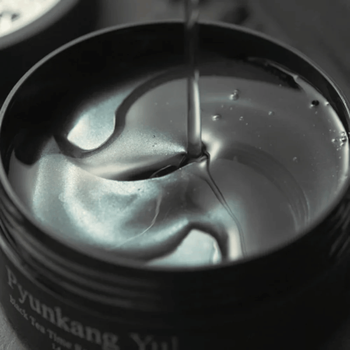 Nærbilde av svarte hydrogel eye patches i en åpen krukke fra Pyunkang Yul. De glansfulle patchene ligger i serum og fremhever produktets fuktighetsgivende og eksklusive følelse.