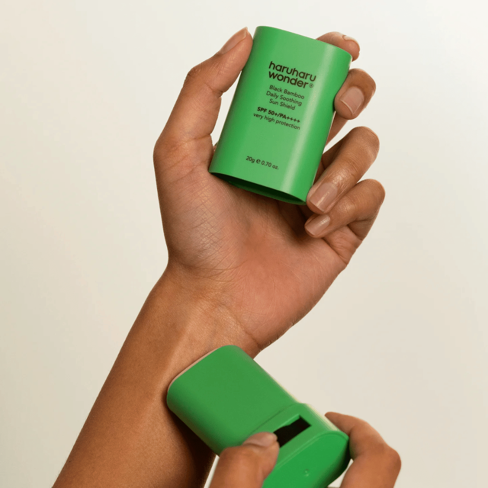 En person påfører Haruharu Wonder Black Bamboo Daily Soothing Sun Shield – en grønn solbeskyttelsesstift med SPF 50+ PA++++ – på håndleddet.