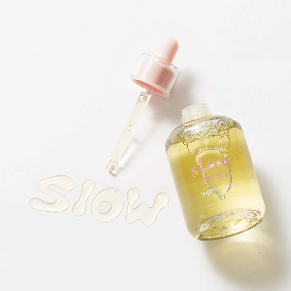 Slow Pure Brightening Tone Serum med åpen pipette, tekst skrevet i serum på overflaten: "Slow".