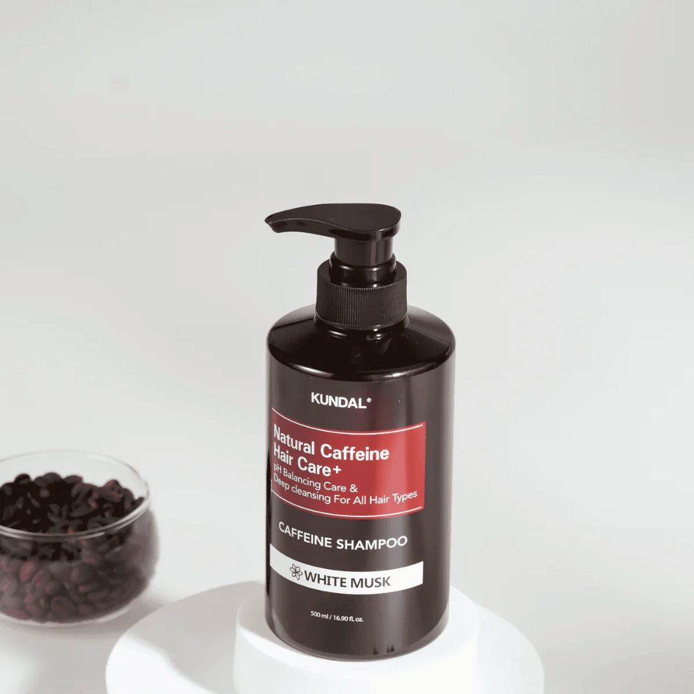 KUNDAL Natural Caffeine Hair Care+ Shampoo White Musk i svart pumpeflaske, 500 ml, plassert ved siden av en bolle med kaffebønner.