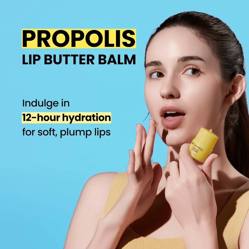 En kvinne påfører CNP Laboratory Propolis Lip Butter Balm, fremhevet mot en blå bakgrunn. Produktet lover 12 timers fuktighet for myke og fyldige lepper, som vises med en gul tube hun holder i hånden.