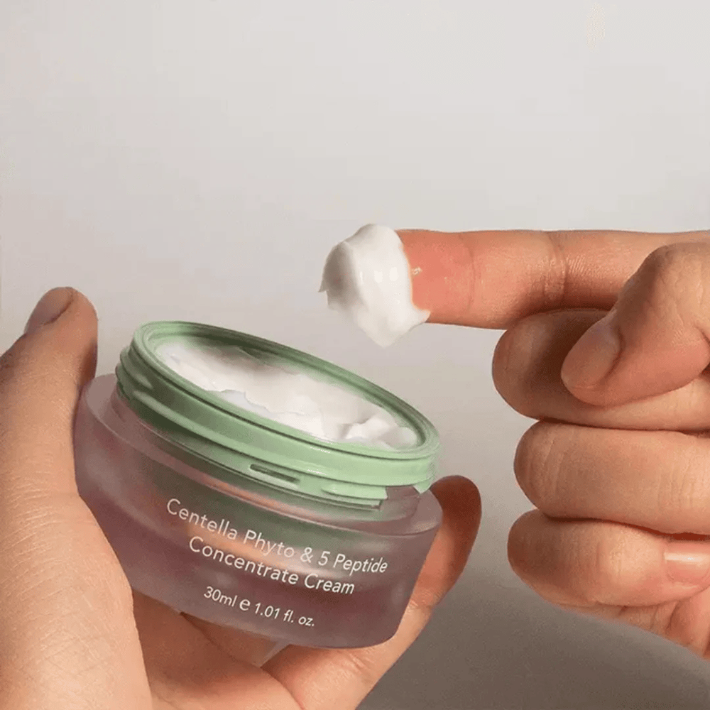 Hånd som tar en klikk Centella Phyto & 5 Peptide Concentrate Cream fra en boks.