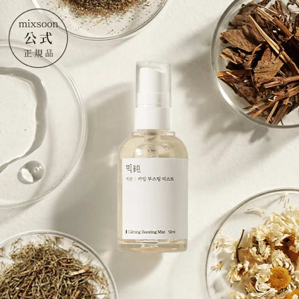 En gjennomsiktig sprayflaske med etiketten 'Calming Boosting Mist' fra Mixsoon, omgitt av tørkede urter og blomster på hvite skåler mot en beige bakgrunn, som fremhever produktenes naturlige ingredienser.