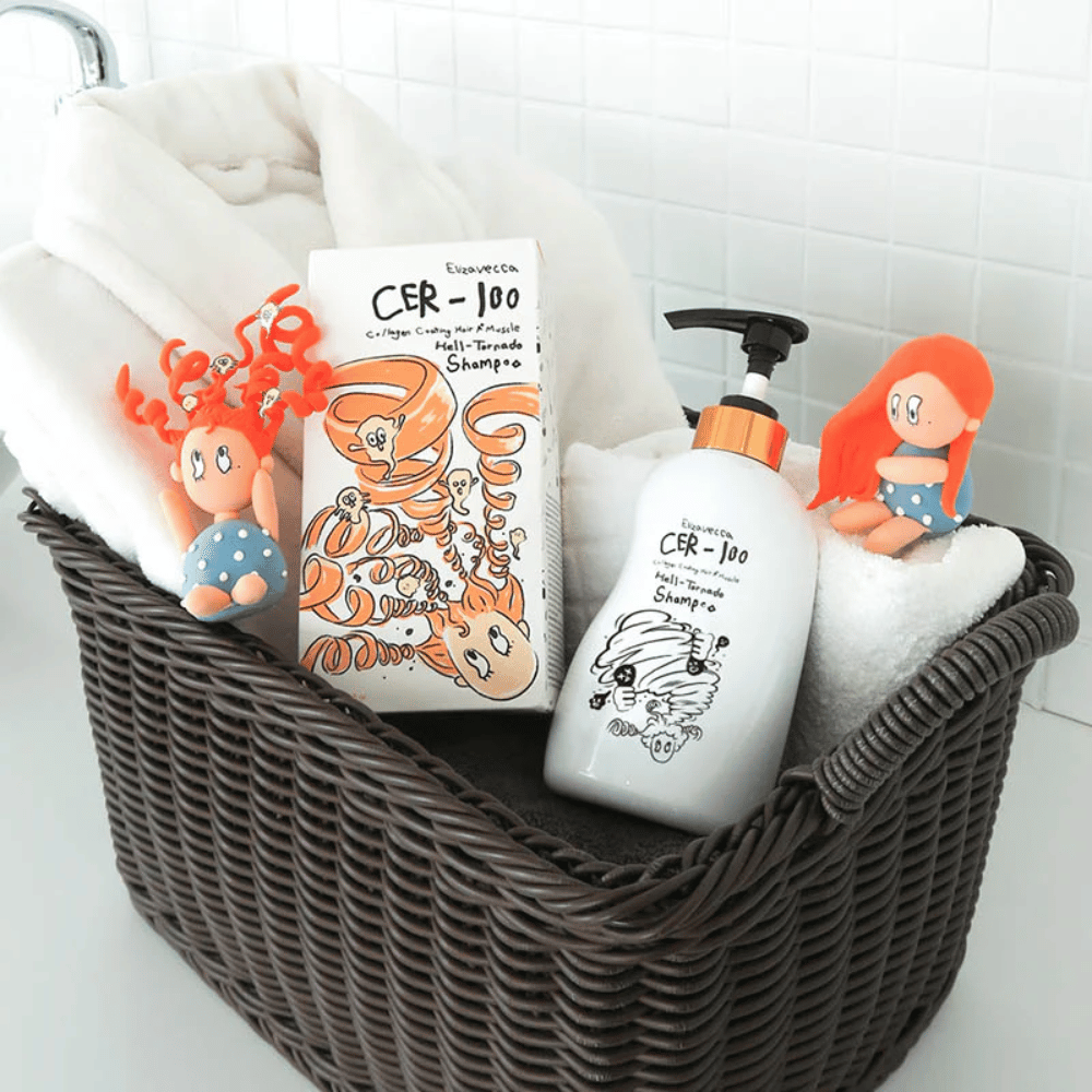 Presentasjonsbilde med Elizavecca CER-100 Shampoo og produktemballasje plassert i en kurv sammen med håndklær. Lekne figurer fra emballasjedesignet fremhever merkets unike og kreative stil.