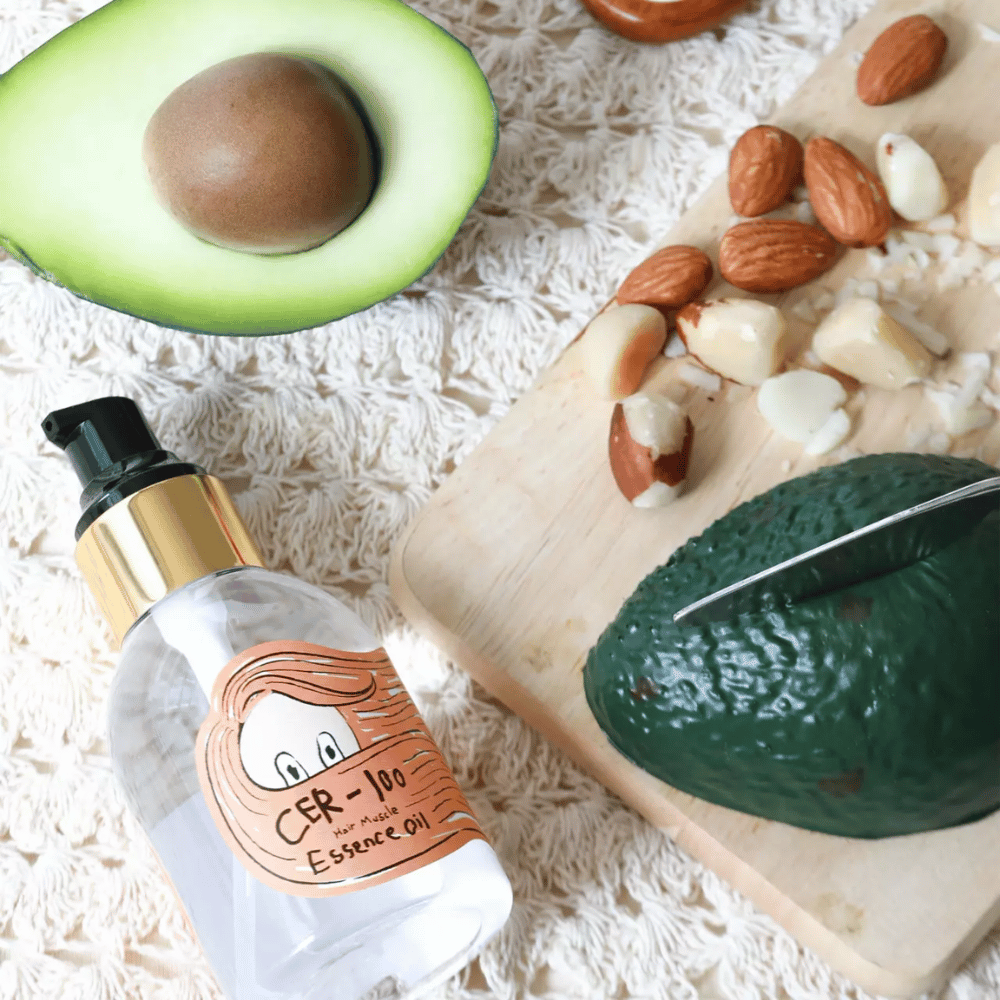 Elizavecca CER-100 Hair Muscle Essence Oil ingredienser – nærbilde med avokado og planteoljer som viser en næringsrik hårolje som hjelper til med å mykgjøre og pleie håret.