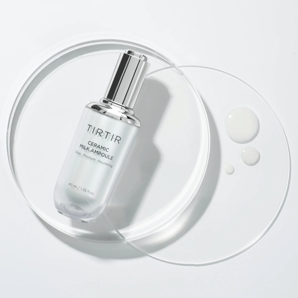 En transparent flaske TIRTIR Ceramic Milk Ampoule på en glassplate med dråper, mot en hvit bakgrunn, fremhever glød, fuktighet og næring.