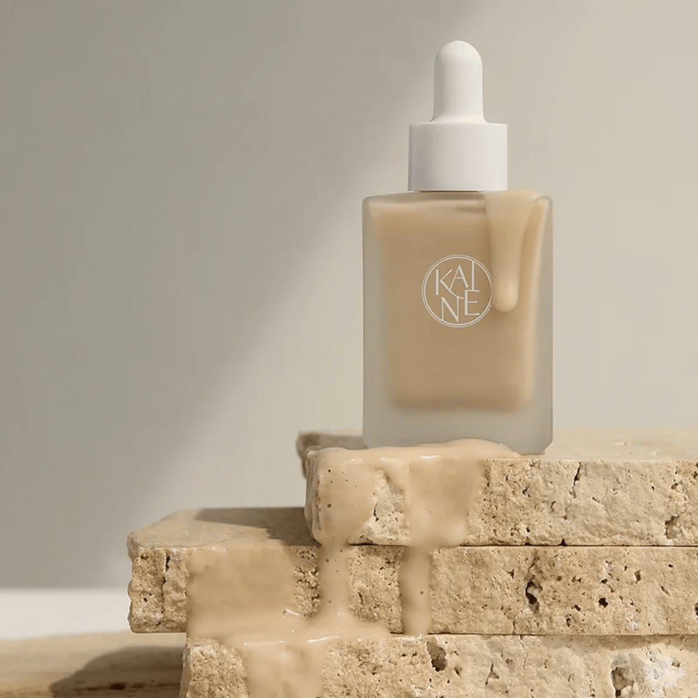 KANE Chaga Collagen Charging Serum i en frostet glassflaske med pipette. Kremet tekstur renner ned over naturlige steiner i et mykt og minimalistisk lys.