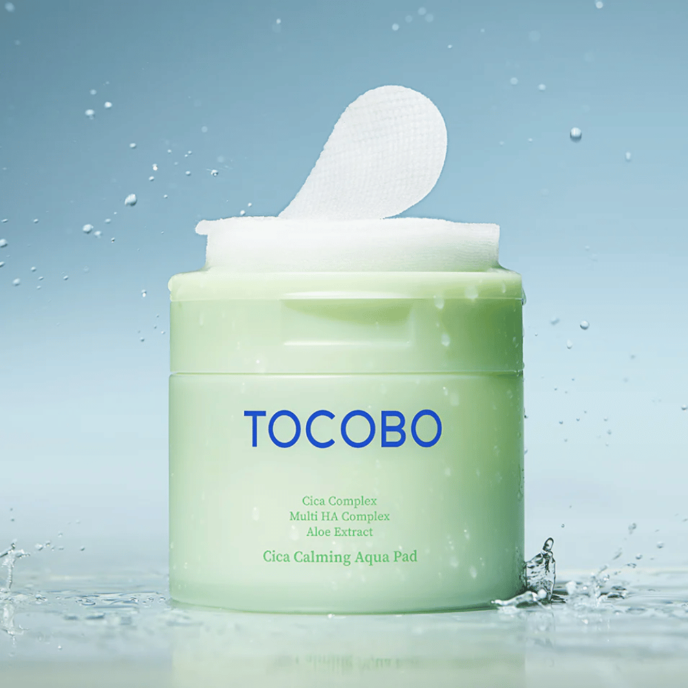 Åpen krukke med TOCOBO Cica Calming Aqua Pad der en toner pad stikker opp fra emballasjen. Vanndråper rundt produktet forsterker følelsen av intensiv fuktighet og friskhet.