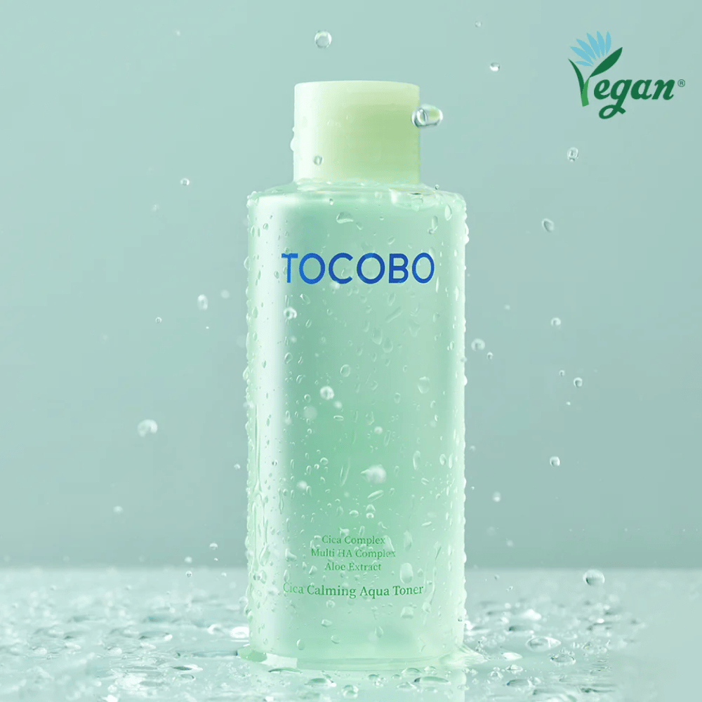 Produktbilde av TOCOBO Cica Calming Aqua Toner omgitt av vanndråper som fremhever tonerens fuktgivende og beroligende egenskaper for sensitiv hud.