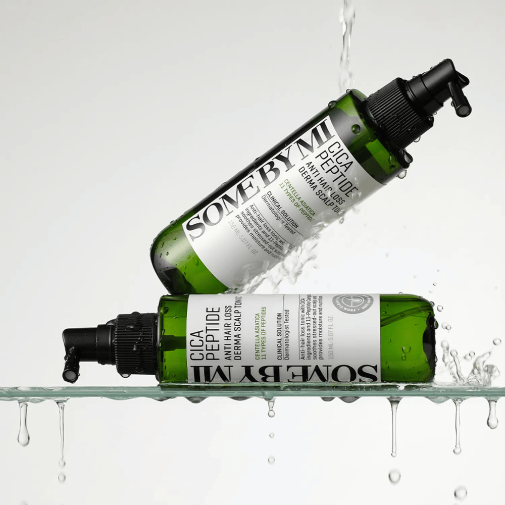 To flasker SOME BY MI Cica Peptide Anti Hair Loss Derma Scalp Tonic ligger i og over vann med dråper som spruter, grønne flasker med svart spraymunnstykke og hvit etikett.