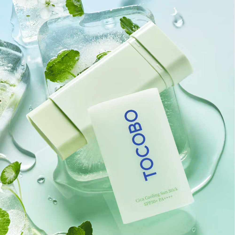 Tocobo Cica Cooling Sun Stick SPF50+ PA++++ på isbiter med grønne planteblader, som gir en kjølende og oppfriskende følelse.