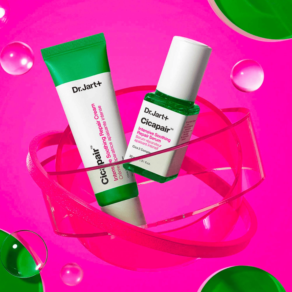 Dr.Jart+ Cicapair Intensive Soothing Repair Cream og Serum i grønne pakninger, som står på en rosa sirkulær base. Produktene er utviklet for å berolige og reparere irritert hud.