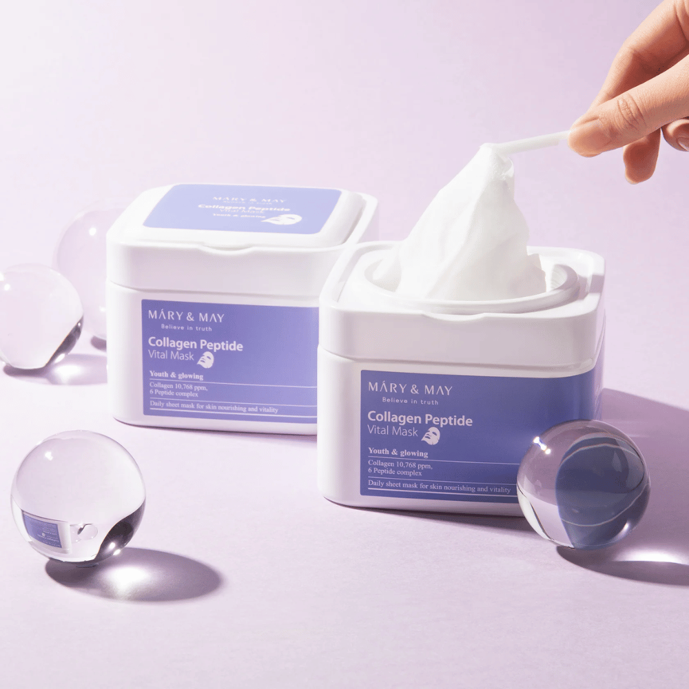 En hånd tar opp en maske fra en krukke med MARY & MAY Collagen Peptide Vital Mask. Masken er ment for daglig bruk for å gi næring og glød til huden, med kollagen og peptider for å støtte hudens ungdommelighet.