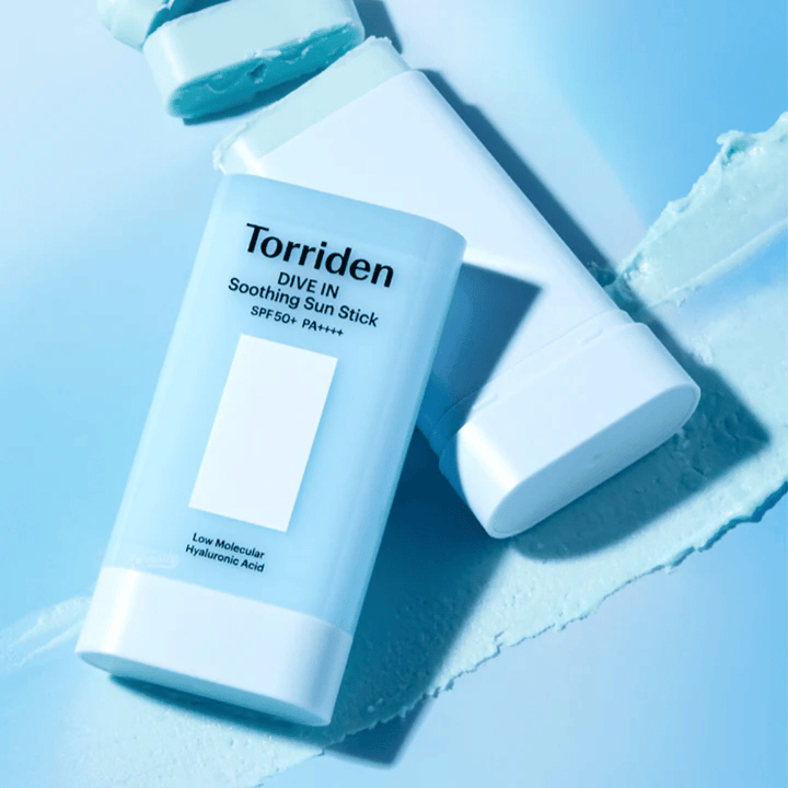 Torriden DIVE IN Soothing Sun Stick SPF50+ PA++++ sammen med utsmurt produkttekstur som illustrerer den fuktighetsgivende og lette påføringen.