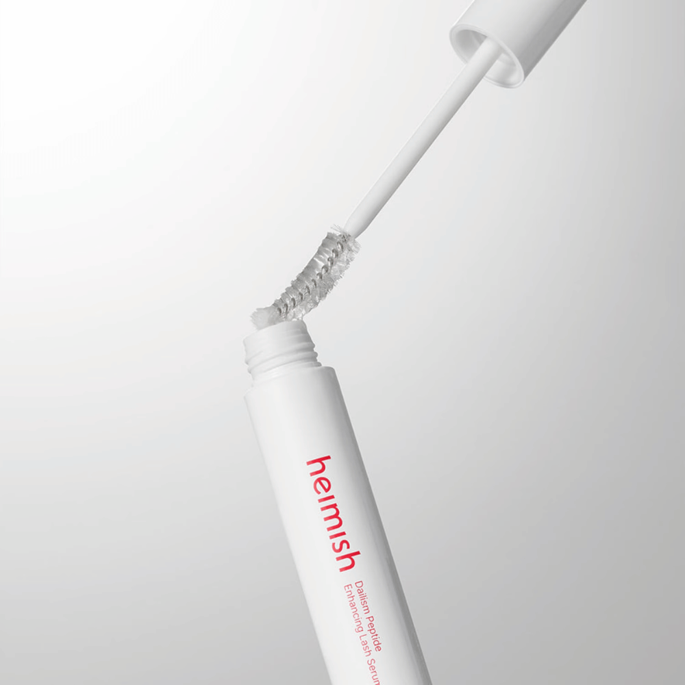 Nærbilde av applikatoren til Heimish Dailism Peptide Enhancing Lash Serum. Børsten trekkes opp fra den hvite beholderen og viser den transparente serumformelen som påføres vippene.
