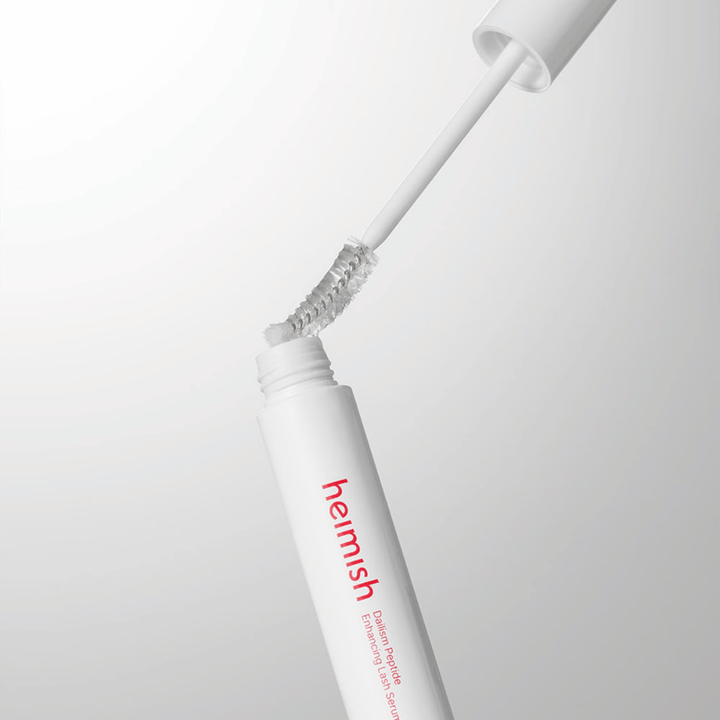 Nærbilde av applikatoren til Heimish Dailism Peptide Enhancing Lash Serum. Børsten trekkes opp fra den hvite beholderen og viser den transparente serumformelen som påføres vippene.
