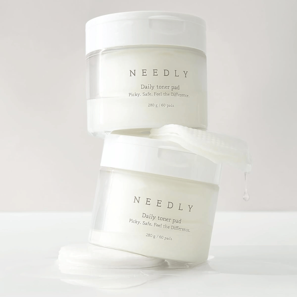 To bokser med Needly Daily Toner Pad stablet oppå hverandre. Boksene er hvite med minimalistisk tekst og inneholder 60 tonerpads hver. En tonerpad ligger delvis utenfor den øvre boksen med væske som drypper av.