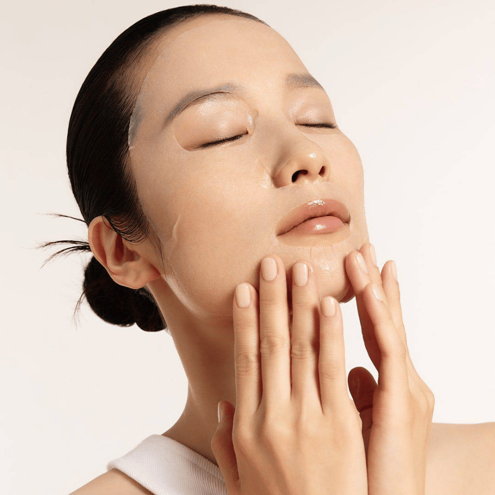 Modell med fuktet og strålende hud påfører Sheet mask, fokus på glød, jevn hudtone og glans.