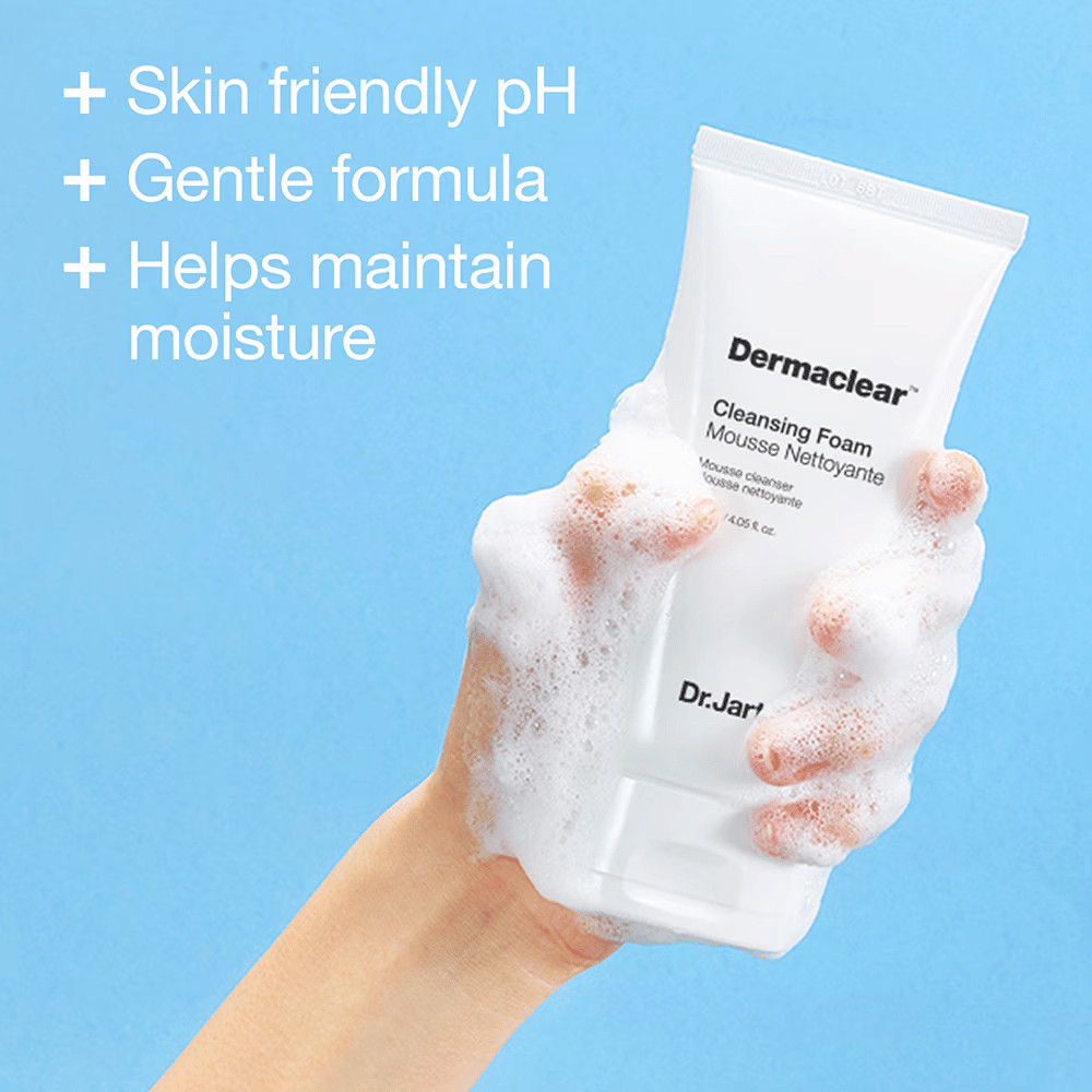 Hånd dekket av skum holder i Dr.Jart+ Dermaclear Cleansing Foam mot blå bakgrunn, med tekst som fremhever hudvennlig pH, mild formel og fuktighetsbevarende egenskaper.